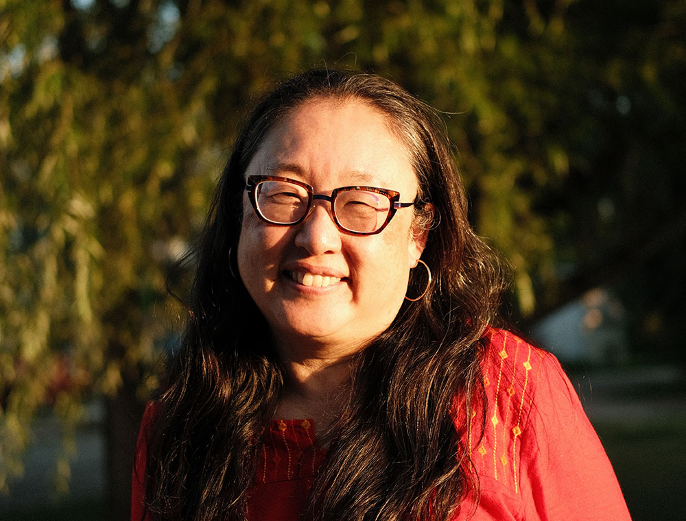 Photo: Sally Ito wearing a red blouse with trees in the background.